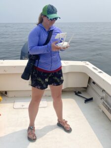 Julia controls a drone flying over open ocean. Once she spots a whale, she sends the drone 100-120 feet high and aims for the perfect shot. All work was conducted in compliance with federal research permits